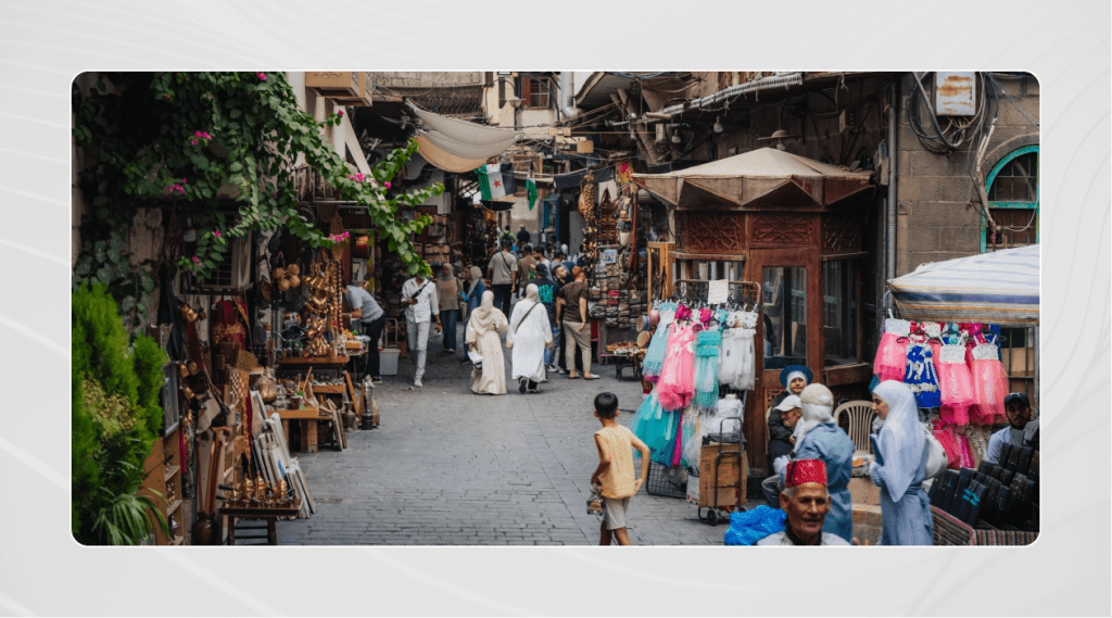 Crowds walk through Souk al-Khayyatin, the historic tailors’ market in the Old City of Damascus, lined with shops selling textiles, clothing, and traditional goods.